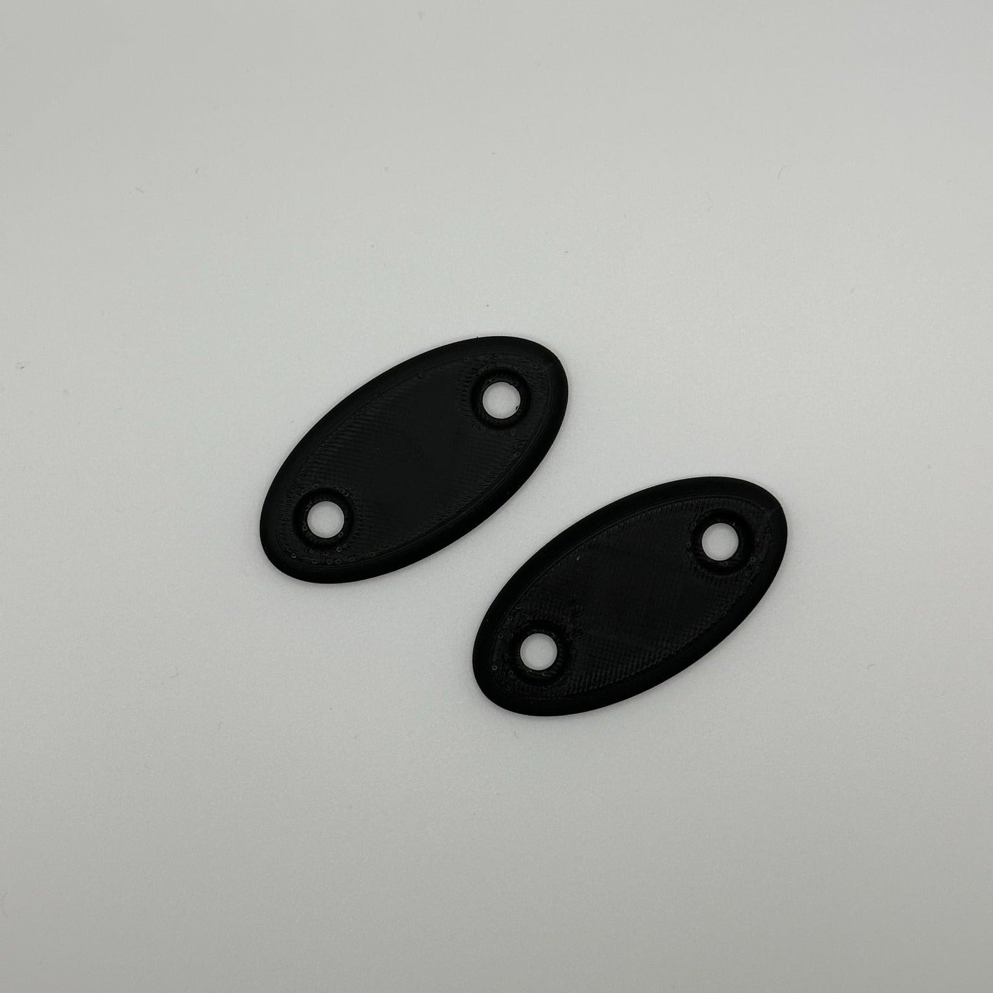 Bovenaanzicht van twee zwarte ovale plaatjes, 3D-geprint met gladde afwerking.